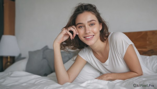 1girl,solo,long hair,looking at viewer,smile,open mouth,blue eyes,brown hair,shirt,white shirt,short sleeves,lying,teeth,indoors,grin,blurry,lips,fingernails,pillow,bed,depth of field,blurry background,on bed,on stomach,t-shirt,messy hair,freckles,realistic,blanket,lamp,ring