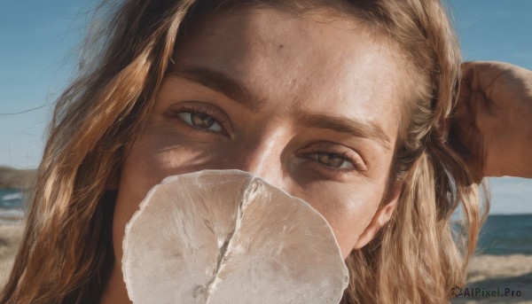 1girl,solo,long hair,looking at viewer,blonde hair,brown hair,brown eyes,outdoors,sky,day,mole,blurry,blue sky,eyelashes,blurry background,ocean,beach,thick eyebrows,portrait,close-up,forehead,freckles,realistic,sand,covered mouth,mole on cheek,arm up,mask,mouth mask