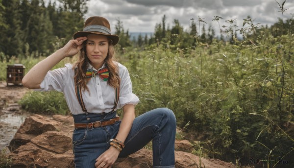 1girl,solo,long hair,looking at viewer,smile,brown hair,shirt,hat,bow,brown eyes,jewelry,sitting,closed mouth,white shirt,outdoors,sky,day,striped,collared shirt,belt,pants,cloud,bowtie,blurry,bracelet,tree,ring,suspenders,cloudy sky,denim,nature,sleeves rolled up,freckles,knee up,jeans,striped bow,rock,realistic,hand on headwear,adjusting headwear,short sleeves,hand up,lips,blurry background,grass,plant,scenery,forest