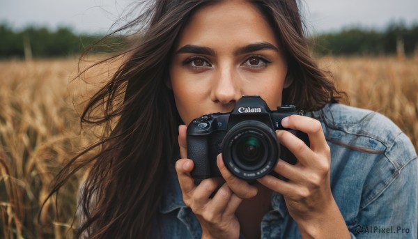 1girl,solo,long hair,looking at viewer,brown hair,shirt,holding,brown eyes,jacket,upper body,outdoors,day,blurry,depth of field,blurry background,thick eyebrows,denim,wind,freckles,jeans,realistic,camera,field,holding camera,denim jacket