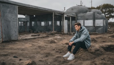 solo,short hair,brown hair,long sleeves,1boy,sitting,jacket,male focus,outdoors,shoes,day,pants,hood,tree,hoodie,black pants,white footwear,hood down,blue jacket,building,sneakers,grey jacket,wide shot,photo background,black hair,sky,scenery,realistic,ruins,grey sky