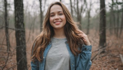 1girl,solo,long hair,looking at viewer,smile,open mouth,brown hair,shirt,long sleeves,brown eyes,jewelry,jacket,white shirt,upper body,outdoors,open clothes,teeth,hand up,necklace,blurry,black eyes,open jacket,tree,dutch angle,blurry background,denim,blue jacket,grey shirt,forehead,realistic,bare tree,denim jacket,day,grin,nature,forest