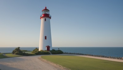 outdoors,sky,day,water,tree,blue sky,no humans,ocean,beach,grass,building,scenery,horizon,clock,road,bush,lamppost,tower,shore,path,lighthouse,sand