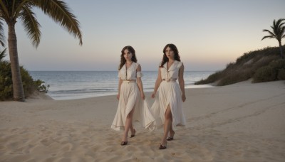 long hair,looking at viewer,smile,multiple girls,brown hair,black hair,dress,2girls,brown eyes,jewelry,closed mouth,standing,full body,short sleeves,outdoors,sky,sleeveless,day,belt,dark skin,water,necklace,white dress,high heels,dark-skinned female,tree,holding hands,ocean,beach,sandals,side slit,walking,skirt hold,sand,palm tree,long dress,arms at sides,horizon,shore,breasts,scenery,sunset,realistic