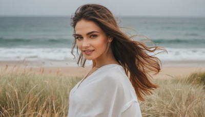 1girl,solo,long hair,looking at viewer,smile,open mouth,brown hair,shirt,brown eyes,white shirt,upper body,outdoors,sky,teeth,day,water,blurry,from side,lips,floating hair,depth of field,blurry background,ocean,upper teeth only,beach,grass,wind,freckles,realistic,nose,horizon,field