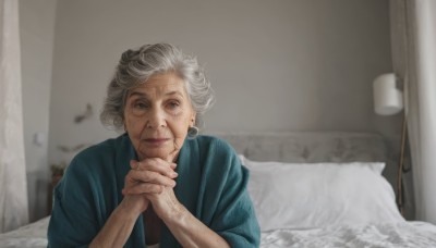 1girl,solo,looking at viewer,smile,short hair,blue eyes,jewelry,closed mouth,upper body,white hair,grey hair,earrings,indoors,blurry,lips,pillow,bed,blurry background,on bed,own hands together,hoop earrings,realistic,lamp,own hands clasped,old,old man,old woman,wrinkled skin,hair bun,blood,green shirt