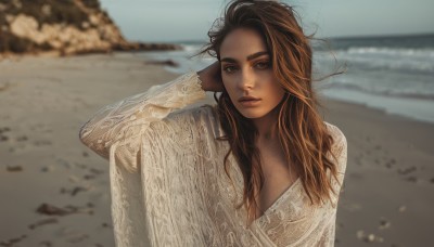 1girl,solo,long hair,breasts,looking at viewer,brown hair,shirt,long sleeves,cleavage,brown eyes,medium breasts,upper body,outdoors,parted lips,day,dark skin,water,blurry,arm up,sweater,dark-skinned female,lips,depth of field,blurry background,ocean,beach,messy hair,freckles,realistic,sand,thick eyebrows,wind,arm behind head,shore