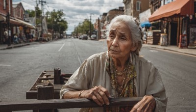 solo,shirt,1boy,jewelry,closed mouth,upper body,white hair,grey hair,male focus,outdoors,sky,day,cloud,necklace,blurry,bracelet,tree,blurry background,facial hair,ring,building,city,realistic,railing,car,road,old,old man,street,photo background,old woman,looking at viewer,smile,holding,brown eyes,japanese clothes,blue sky,depth of field,cloudy sky,ground vehicle,motor vehicle,beard,beads,sign,bead necklace,town,wrinkled skin