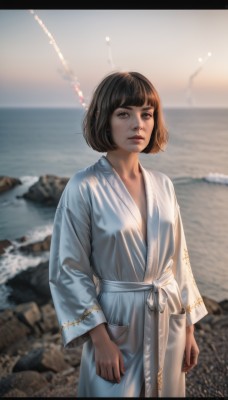 1girl,solo,looking at viewer,short hair,bangs,brown hair,black hair,long sleeves,brown eyes,closed mouth,standing,cowboy shot,outdoors,day,blunt bangs,water,blurry,lips,depth of field,blurry background,ocean,beach,bob cut,letterboxed,robe,rock,realistic,nose,sand,arms at sides,shore,white robe,breasts,small breasts,japanese clothes,artist name,wide sleeves,sash