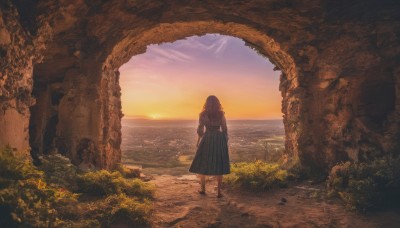 1girl,solo,long hair,skirt,brown hair,shirt,long sleeves,dress,standing,outdoors,sky,cloud,black skirt,water,from behind,tree,blue skirt,ocean,sunlight,grass,plant,scenery,sunset,long skirt,horizon,facing away,wide shot,twilight,shoes,beach,rock,sun,arch