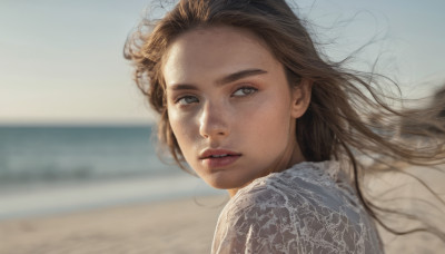 1girl, solo, long hair, looking at viewer, brown hair, shirt, brown eyes, white shirt, upper body, outdoors, parted lips, day, blurry, lips, looking to the side, floating hair, blurry background, beach, wind, freckles, realistic, nose