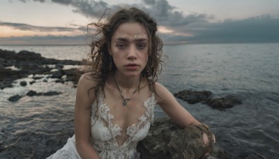 1girl,solo,long hair,breasts,looking at viewer,blue eyes,brown hair,dress,cleavage,bare shoulders,jewelry,medium breasts,collarbone,upper body,earrings,outdoors,parted lips,sky,sleeveless,cloud,dark skin,water,necklace,white dress,blurry,lips,wet,blurry background,ocean,beach,cloudy sky,messy hair,wet clothes,freckles,realistic,horizon,wet hair,dirty,mole,sleeveless dress,rock,waves