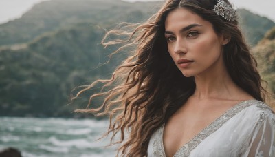 1girl,solo,long hair,breasts,looking at viewer,brown hair,black hair,hair ornament,dress,cleavage,brown eyes,collarbone,upper body,outdoors,white dress,blurry,lips,blurry background,wavy hair,wind,mountain,realistic,nose,flower,day,hair flower,water,floating hair,ocean