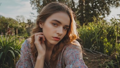 1girl,solo,long hair,looking at viewer,brown hair,brown eyes,jewelry,upper body,flower,earrings,outdoors,sky,day,hand up,necklace,blurry,lips,grey eyes,depth of field,blurry background,wavy hair,floral print,plant,hand on own face,freckles,head rest,realistic,nose,red lips,shirt,makeup,sunlight,thick eyebrows,blue shirt,mole on cheek