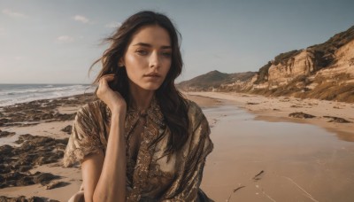 1girl,solo,long hair,breasts,looking at viewer,brown hair,shirt,black hair,cleavage,brown eyes,jewelry,medium breasts,closed mouth,upper body,short sleeves,earrings,outdoors,sky,day,hand up,water,lips,ocean,beach,wind,mountain,realistic,nose,sand,horizon,brown shirt,shore,desert,dress,cloud,scenery