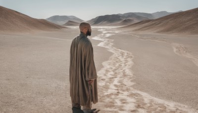 solo,long sleeves,1boy,holding,standing,male focus,outdoors,day,from behind,mask,beach,sandals,scenery,robe,mountain,sand,bald,wide shot,desert,footprints,looking at viewer,short hair,brown hair,sky,shoes,pants,water,black footwear,from side,profile,ocean,cloak,mouth mask,very short hair,mountainous horizon