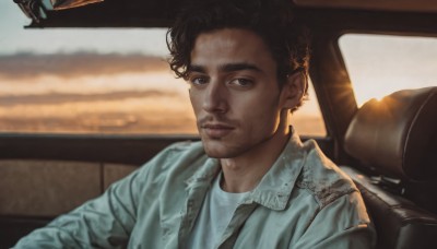 solo,looking at viewer,short hair,brown hair,shirt,black hair,1boy,brown eyes,sitting,closed mouth,jacket,white shirt,upper body,male focus,dark skin,blurry,black eyes,blurry background,facial hair,ground vehicle,motor vehicle,realistic,stubble,car,driving,car interior,afro,lips,thick eyebrows,blue jacket,denim jacket