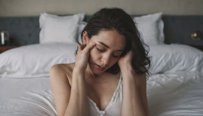 1girl,solo,long hair,breasts,black hair,cleavage,bare shoulders,medium breasts,closed mouth,closed eyes,upper body,lying,indoors,mole,blurry,lips,pillow,bed,blurry background,on bed,messy hair,facing viewer,freckles,mole on breast,realistic,brown hair,depth of field,lamp