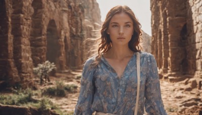 1girl,solo,long hair,looking at viewer,blue eyes,brown hair,shirt,long sleeves,closed mouth,collarbone,upper body,outdoors,day,bag,blurry,lips,depth of field,blurry background,wavy hair,floral print,blue shirt,rock,shoulder bag,realistic,nose,arms at sides,dress,flower,blue dress,expressionless,sunlight,backlighting