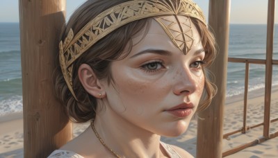 1girl,solo,looking at viewer,short hair,brown hair,brown eyes,jewelry,earrings,outdoors,parted lips,day,water,necklace,hair bun,lips,grey eyes,ocean,beach,piercing,portrait,freckles,circlet,realistic,nose,sand,bangs,closed mouth,hairband,sky,single hair bun