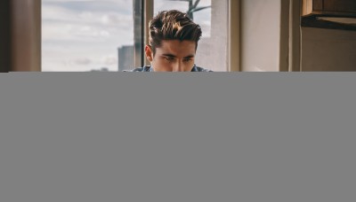 solo,short hair,brown hair,shirt,black hair,1boy,closed mouth,jacket,white shirt,upper body,male focus,open clothes,day,indoors,blurry,open jacket,cup,window,facial hair,table,denim,blue jacket,building,sleeves rolled up,city,realistic,stubble,denim jacket,looking outside,brown eyes,beard,animification,leather jacket